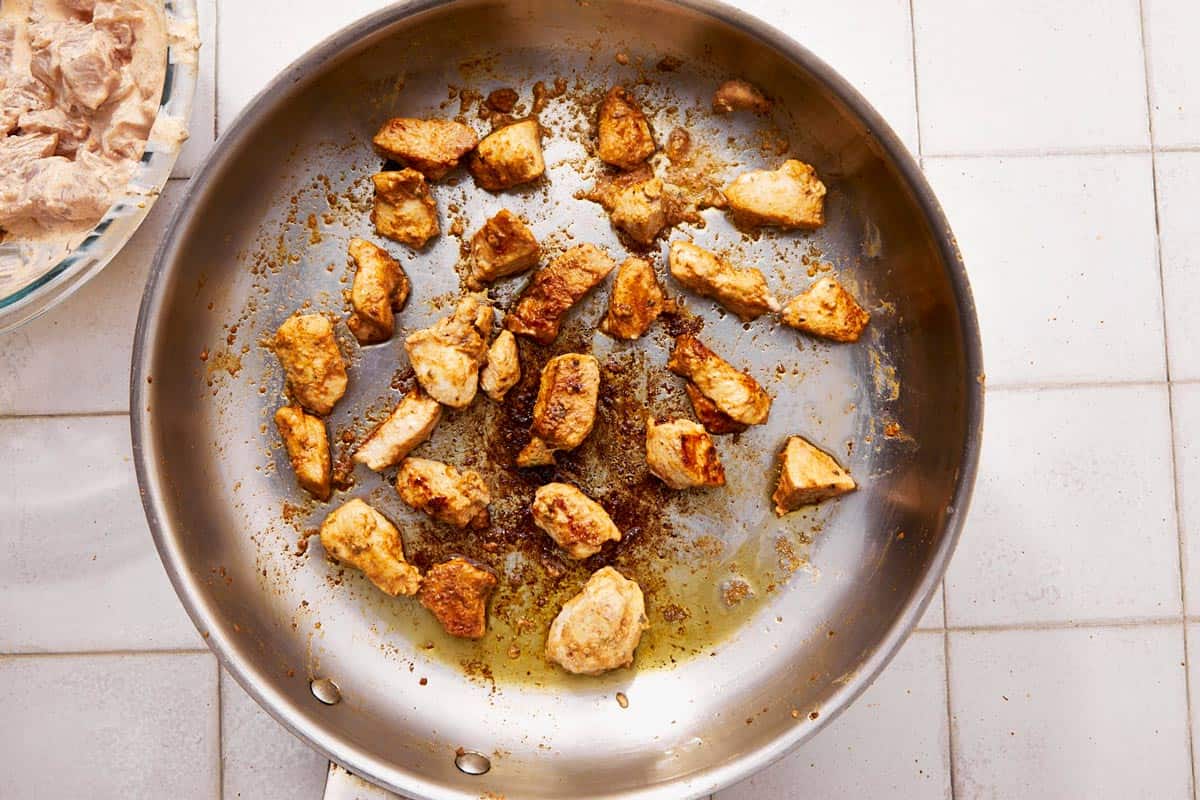 Chicken pieces browning in a stainless steel skillet.

