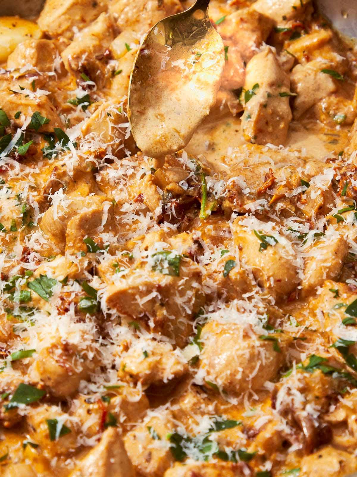 Golden spoon scooping creamy Greek Yogurt Chicken with sun-dried tomatoes and fresh parsley from a rich, velvety sauce.