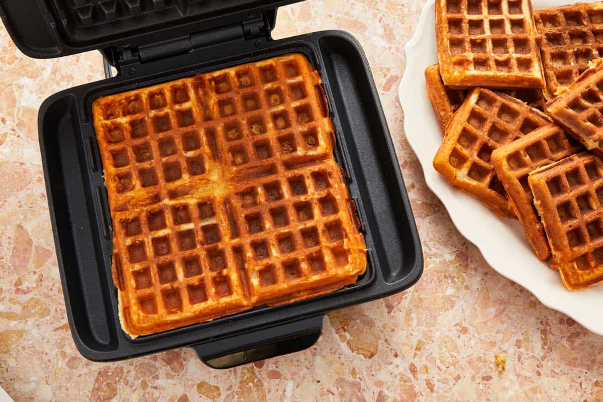 A waffle maker with a freshly cooked waffle inside.