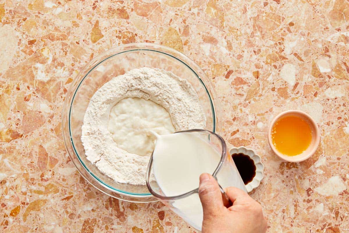 Pouring flour into a bowl with other wet ingredients, preparing to whisk the mixture into a smooth batter.
