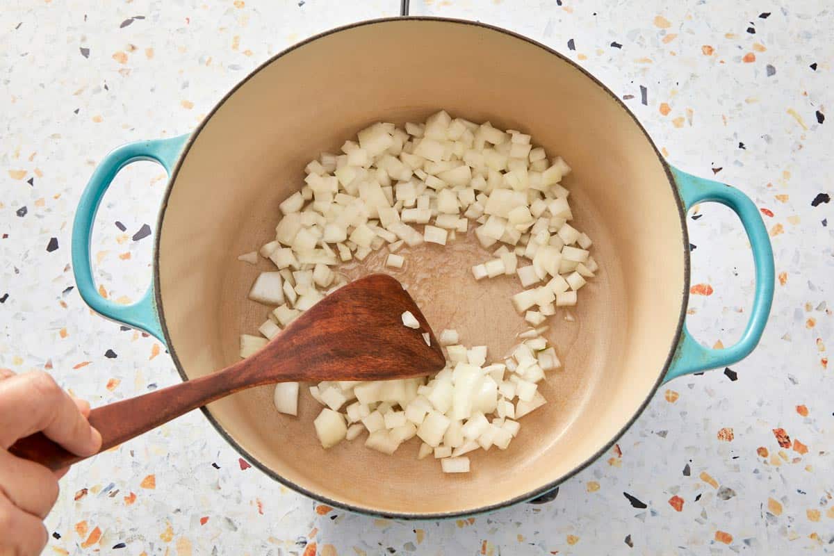 Sautéing chopped onions in a large Dutch oven with a wooden spoon.