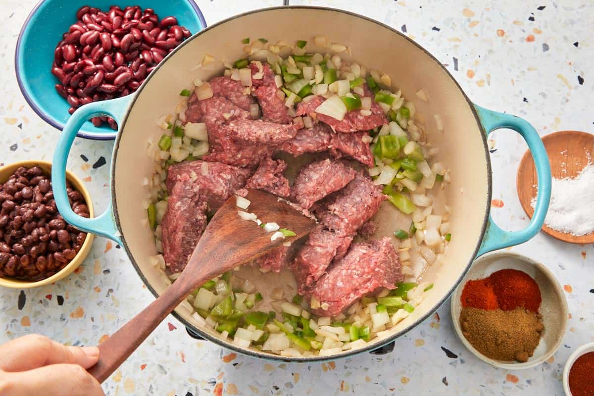 Breaking up ground beef and mixing with onions, peppers, and garlic.