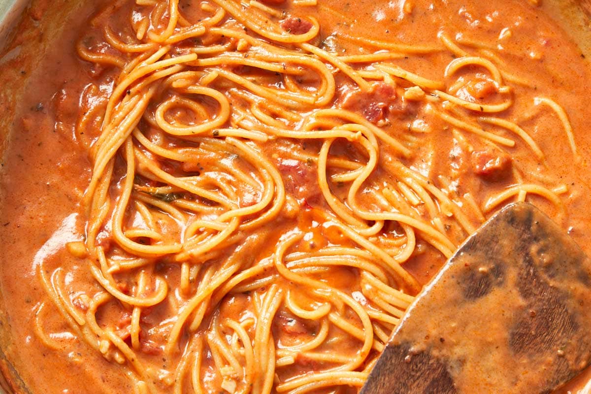 Cooked creamy tomato pasta being plated in generous swirls, rich and velvety.