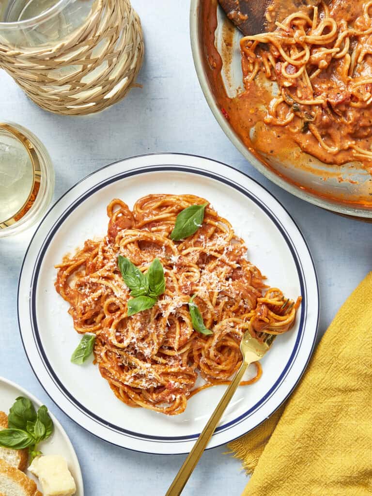 Plate of creamy tomato pasta with fresh basil and parmesan served in a white dish.