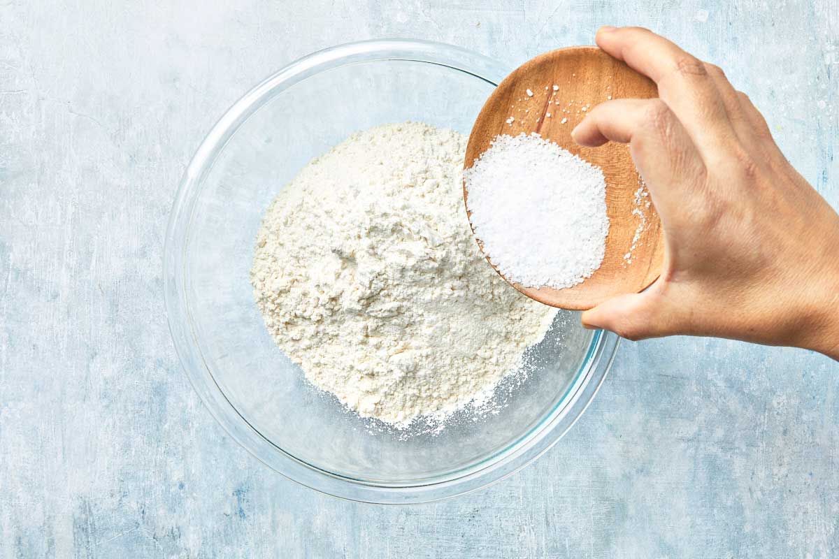 Flour and salt being poured into a large glass bowl.