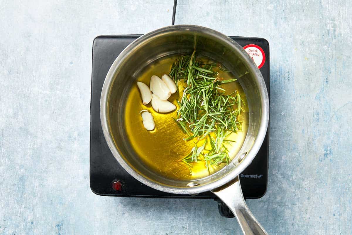 Olive oil infused with rosemary and garlic heating in a small saucepan.
