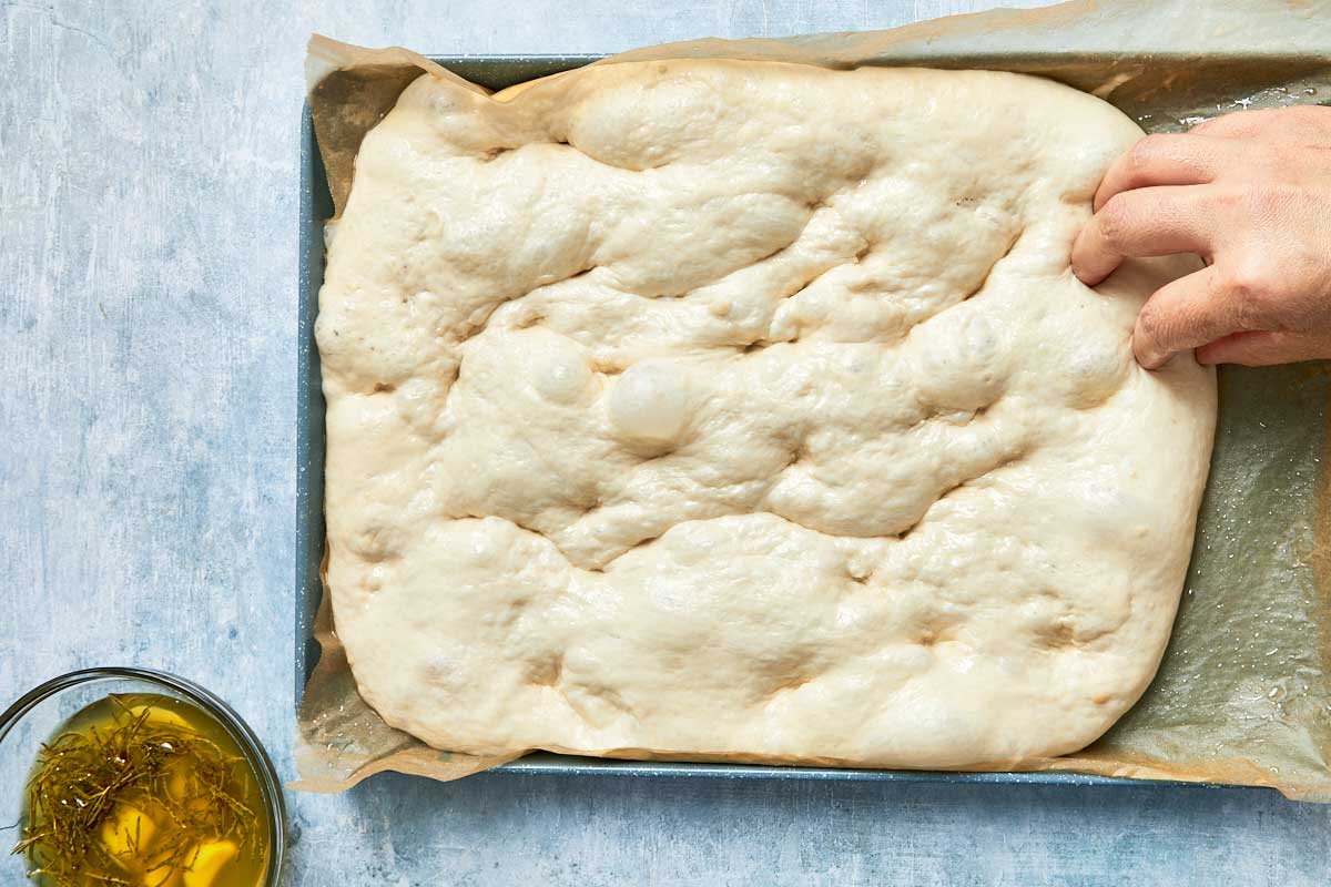 Fingers pressing dimples all over the surface of the rested dough.