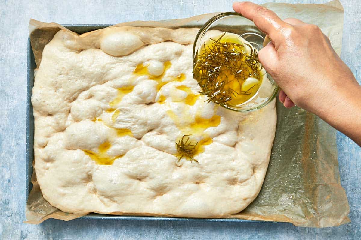 Infused oil being drizzled over dimpled dough before baking.