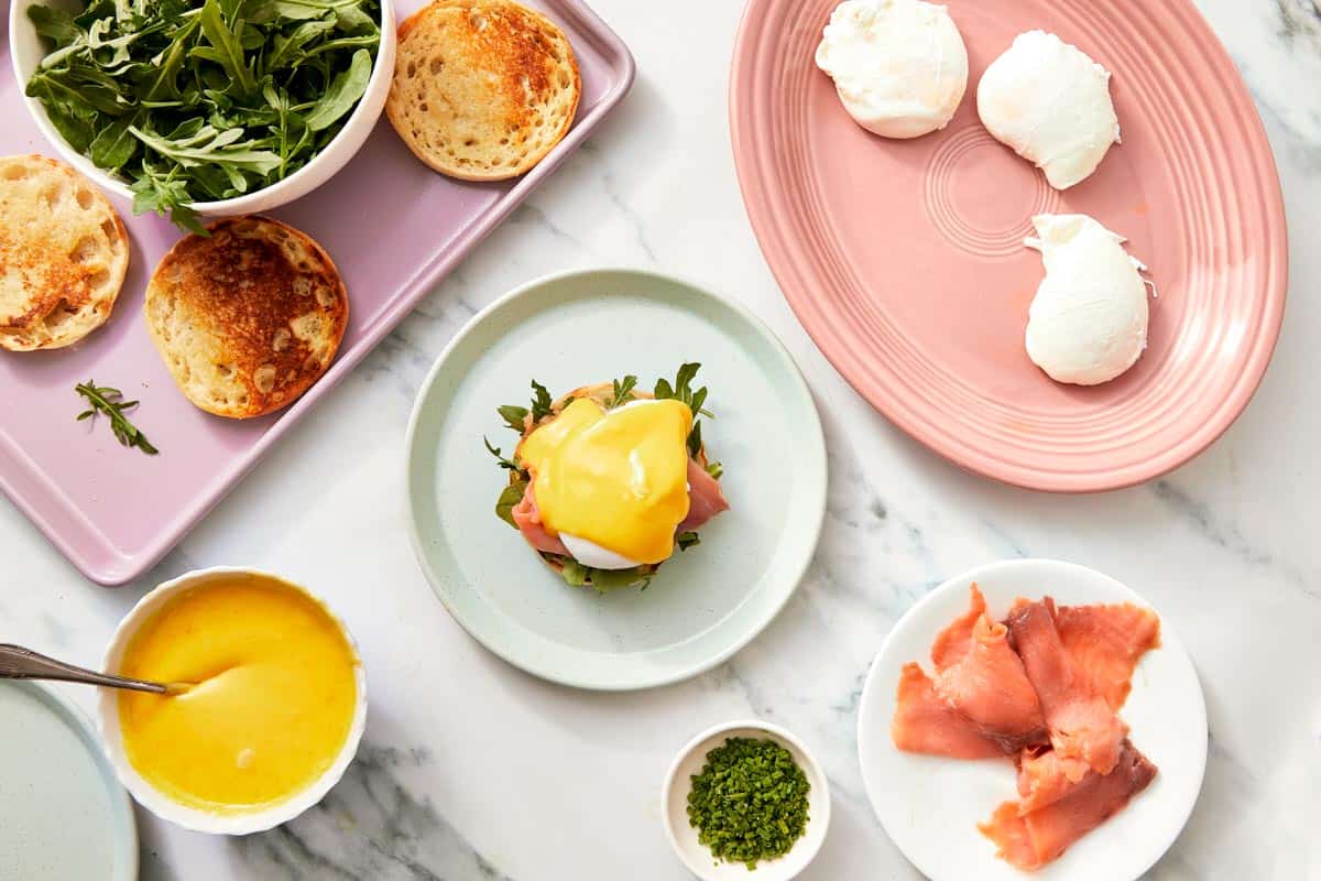A spoonful of hollandaise sauce ready to be poured over the poached eggs, with the full assembly laid out.