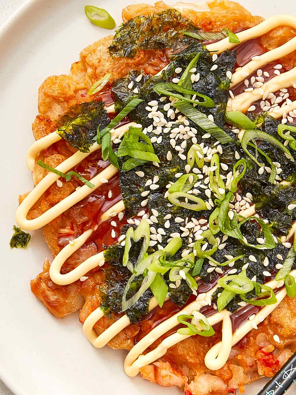 Close-up of okonomiyaki pancake topped with nori, scallions, sesame seeds, and mayo and sauce drizzles.
