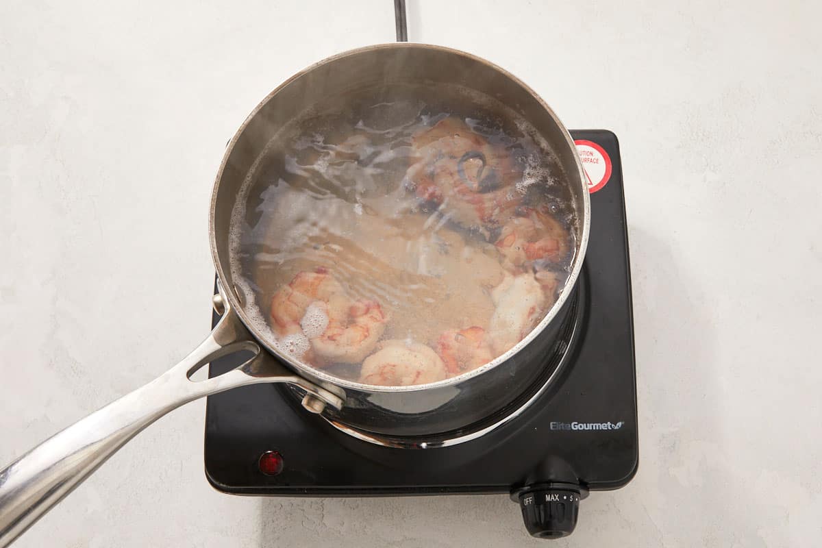 Shrimp boiling in a small pot of water on a burner.