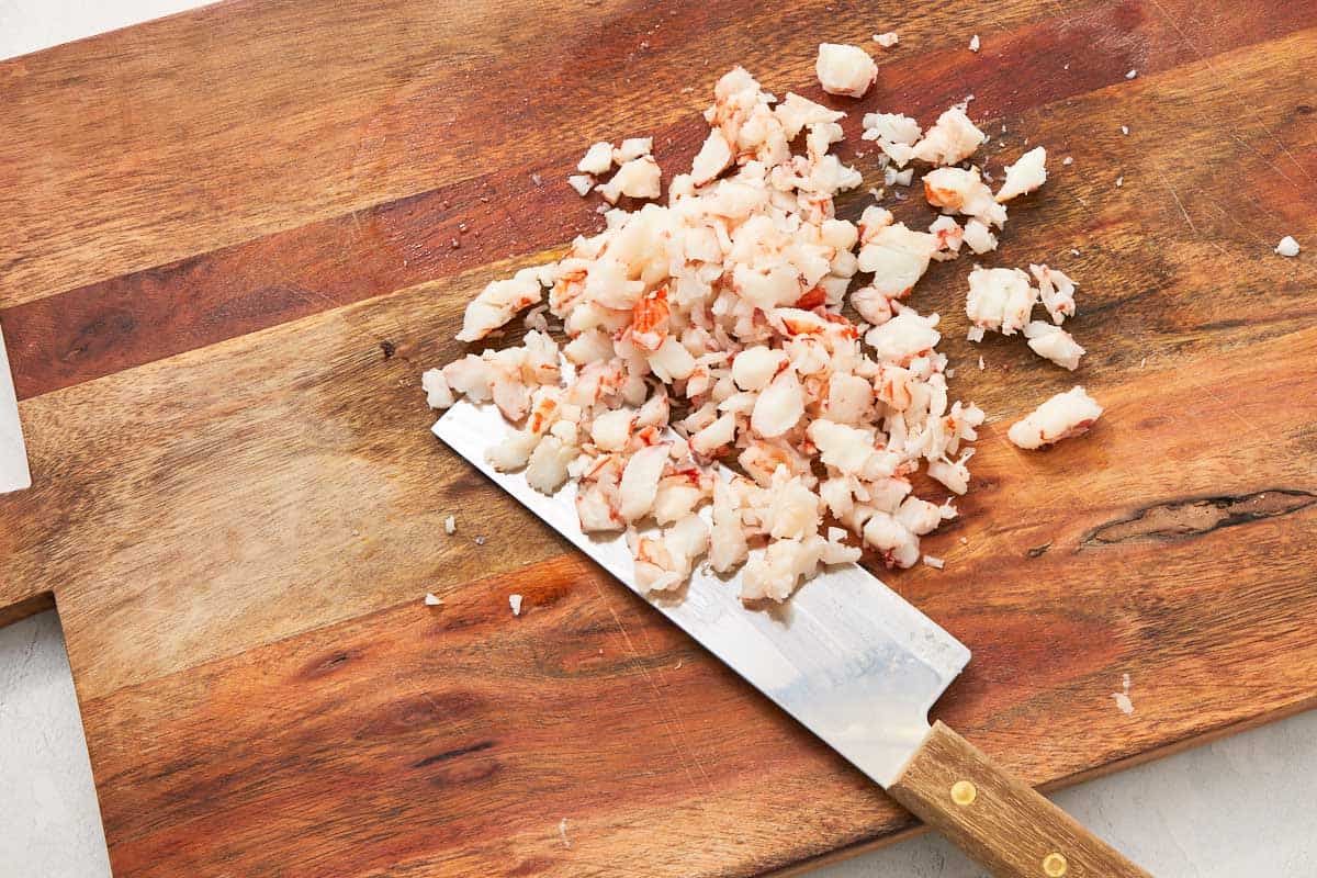 Chopped cooked shrimp on a wooden cutting board with a chef’s knife.
