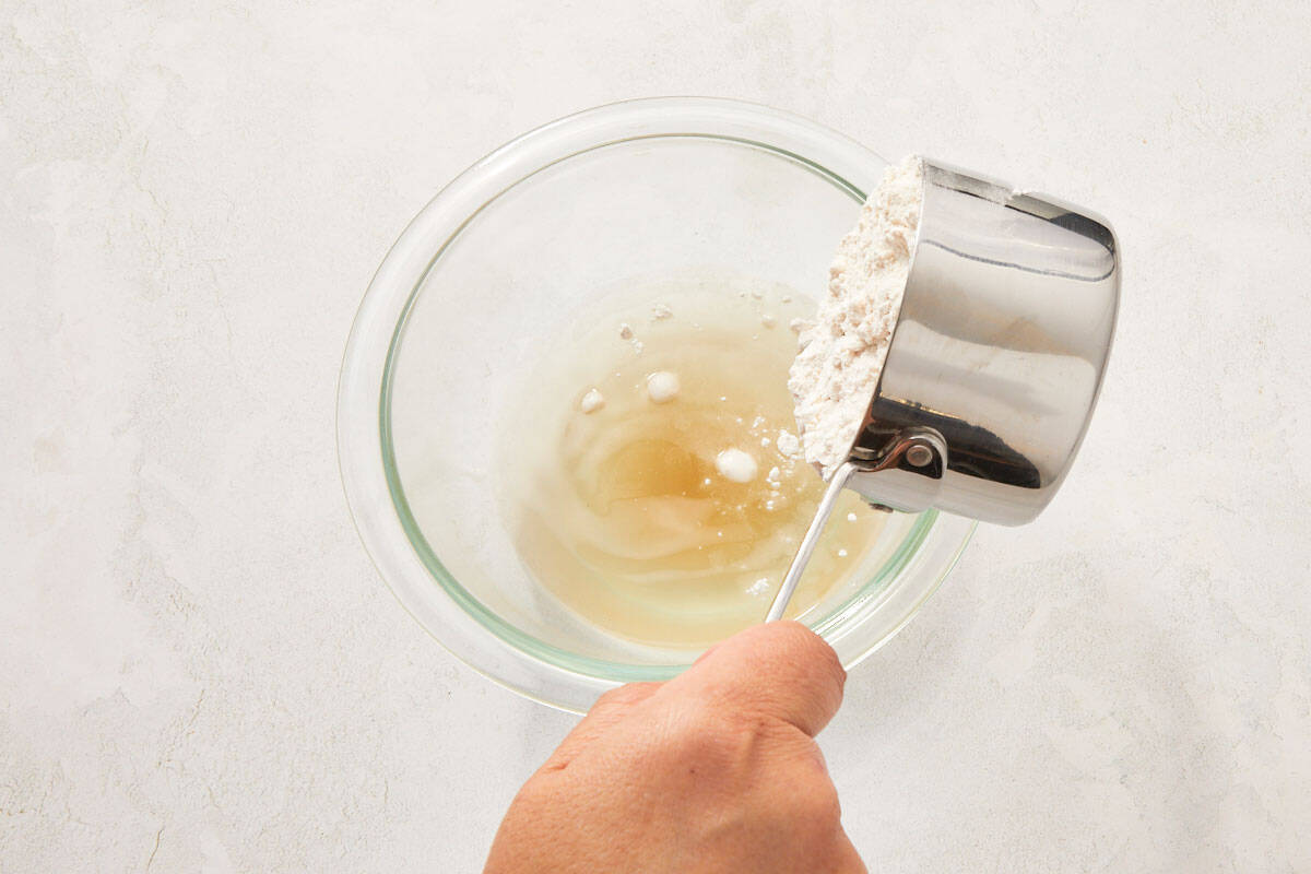 Pouring warm shrimp broth into a glass bowl containing flour.
