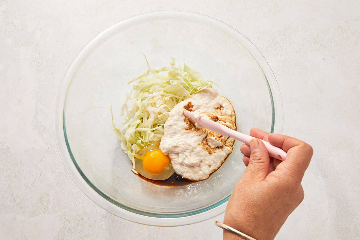 Chopped cabbage and egg being stirred into the batter with a wooden spoon.