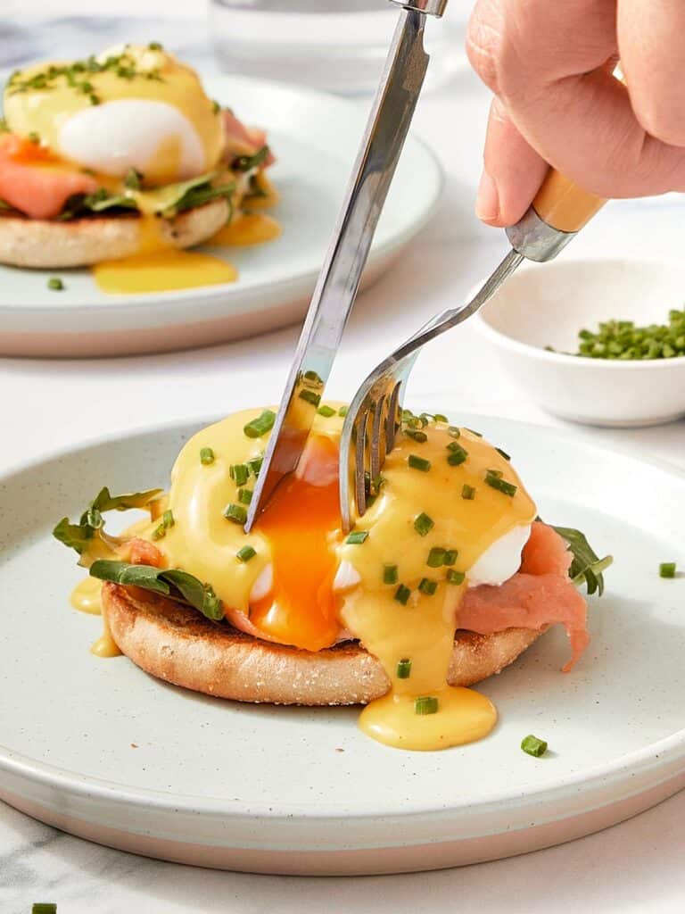 A person cutting a piece of egg on a plate.