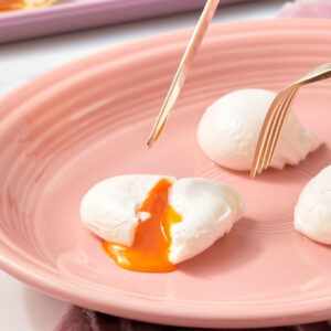 Poached Eggs on a pink plate with a fork.