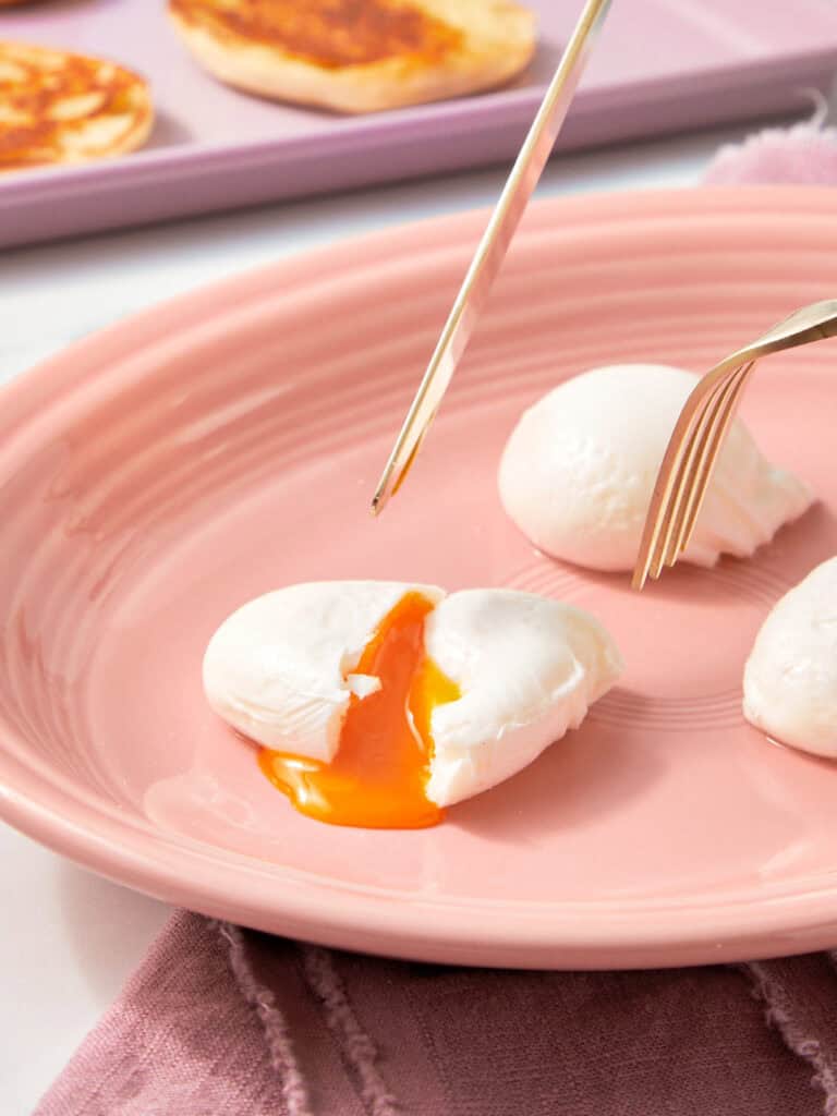 Poached Eggs on a pink plate with a fork.
