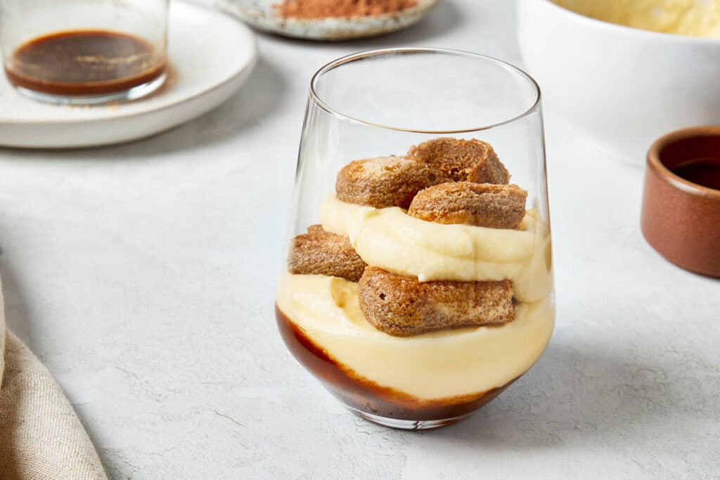 Layers of mascarpone cream and ladyfingers stacked in a glass.