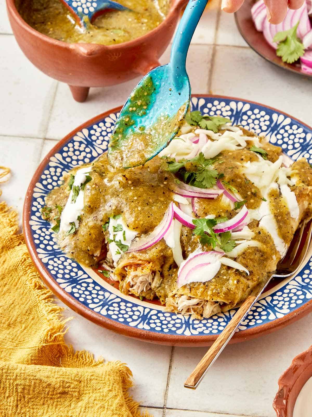 Mexican chicken enchiladas with a blue spoon.