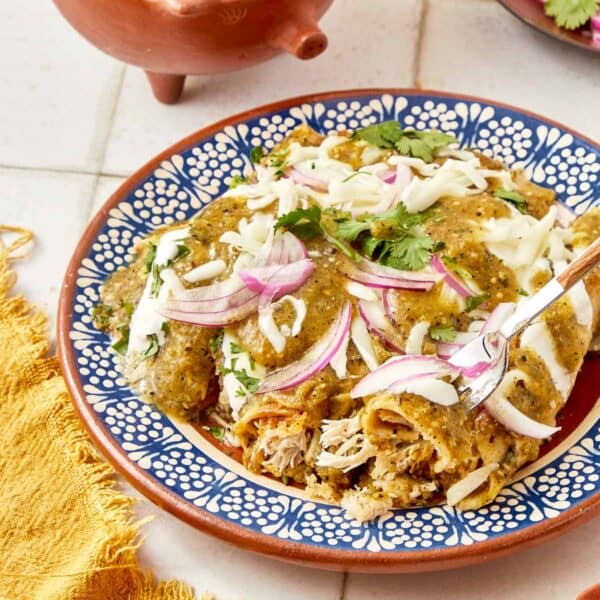 Mexican chicken enchiladas with a blue spoon.