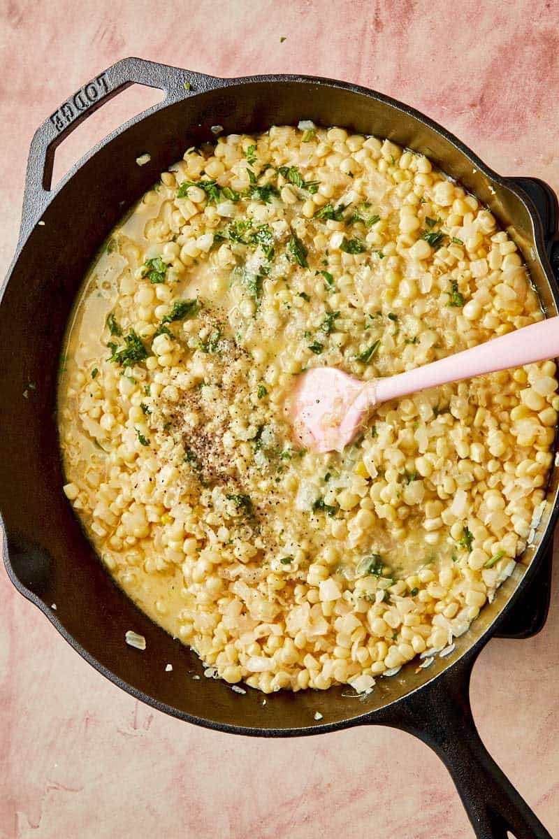 A skillet brimming with creamy corn and cheese, seasoned and kept warm for serving.