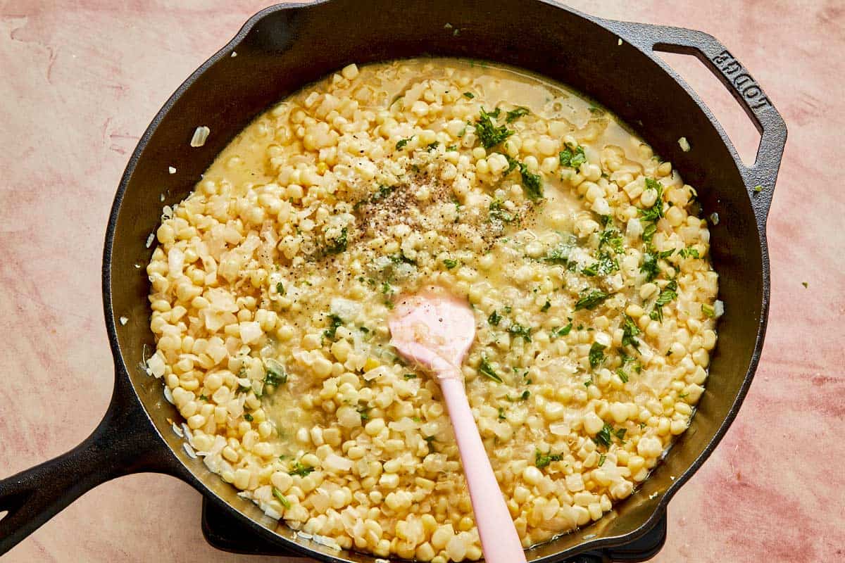 A skillet brimming with creamy corn and cheese, seasoned and kept warm for serving.