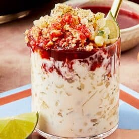 A glass of Esquites with a spoon and lime. - 15