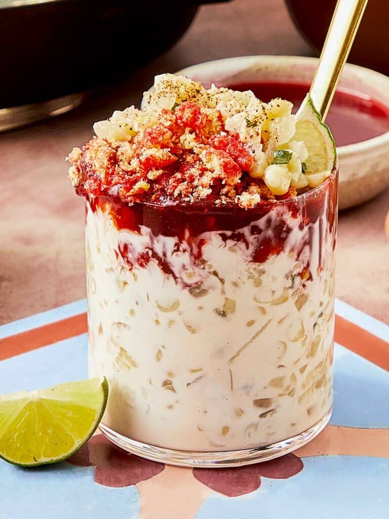 A glass of Esquites with a spoon and lime.