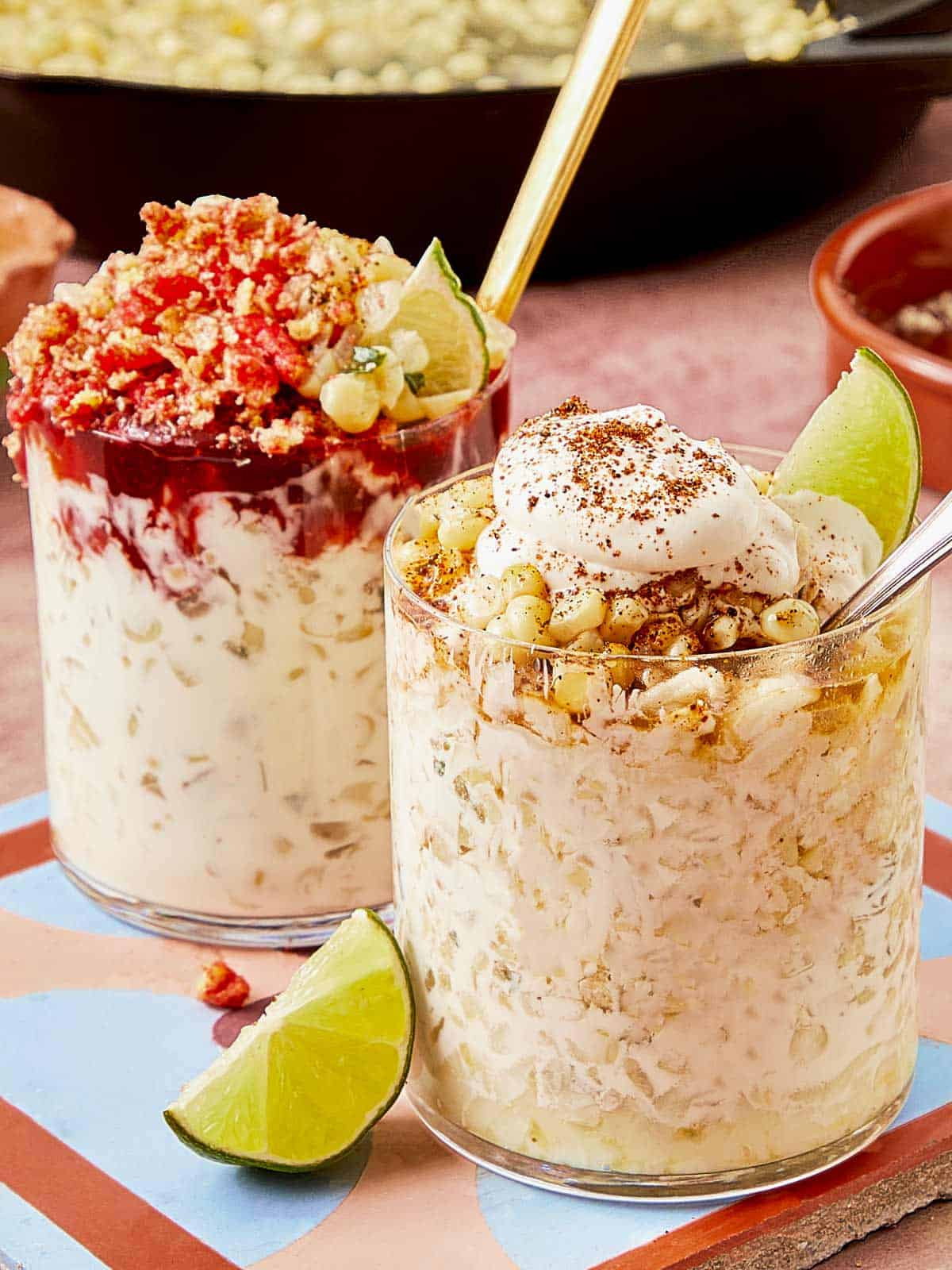 Two glasses of Esquites with a spoon and lime.