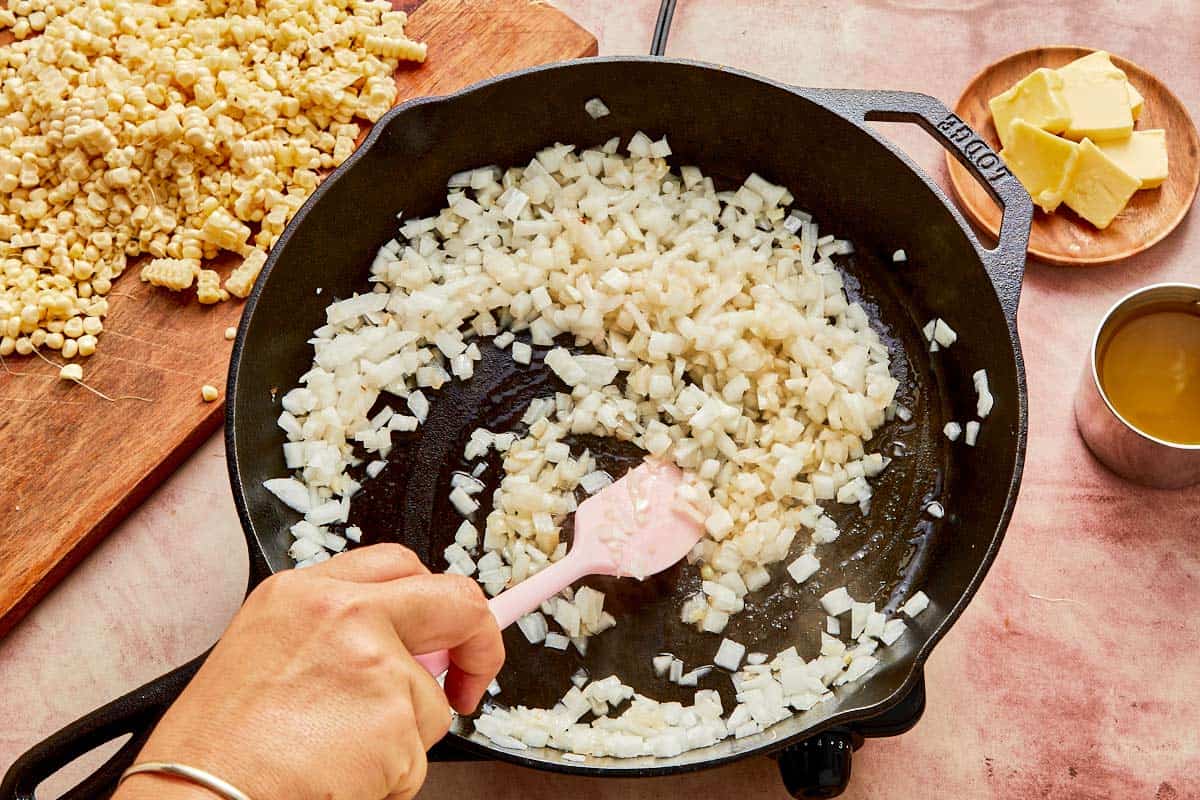 A cook stirring onions in a skillet with butter, preparing a flavorful base for a dish.