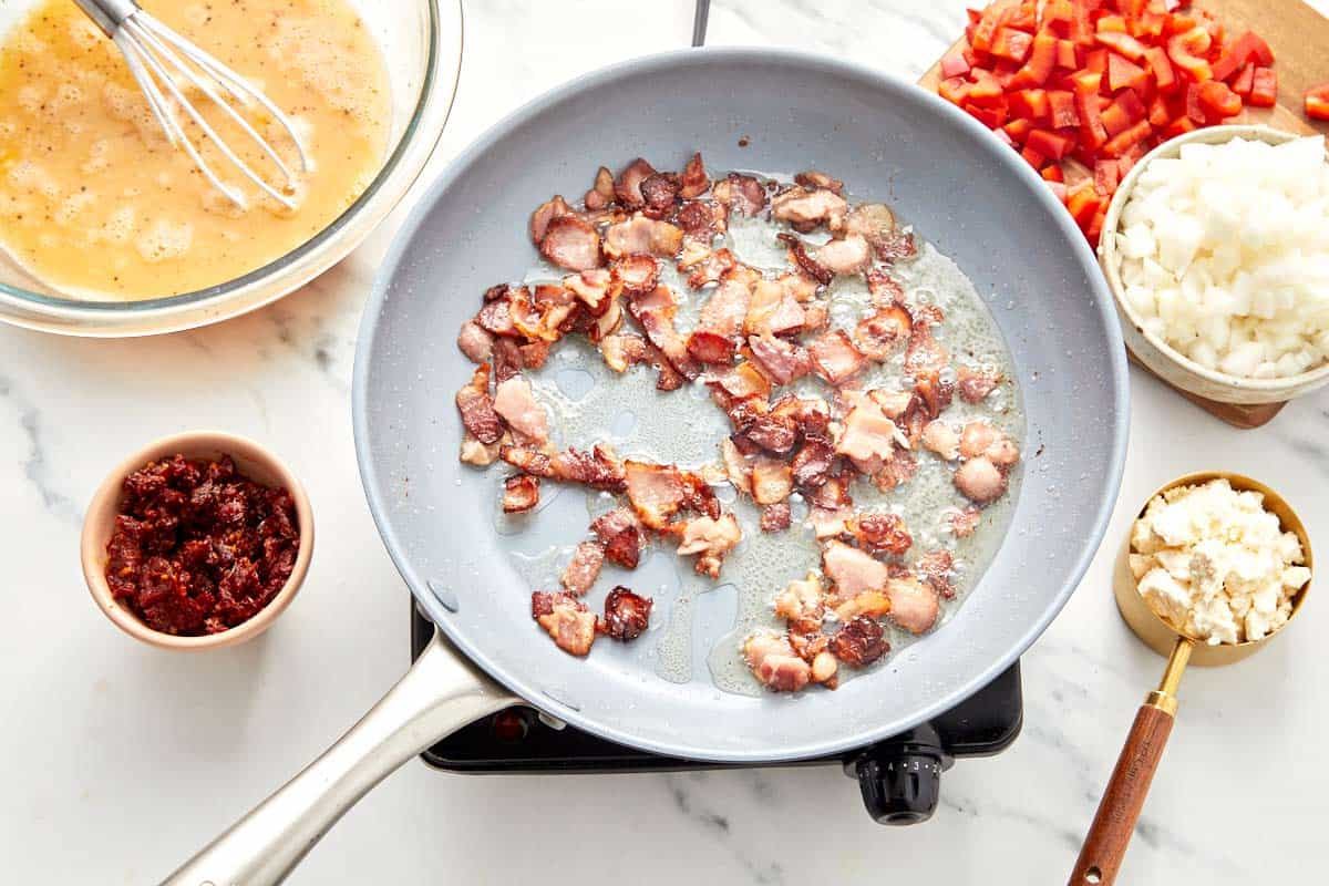 Diced bacon cooking in a skillet until golden and crisp.