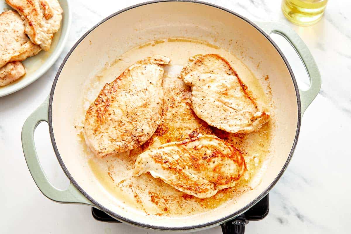 Golden seared chicken cooking in a hot skillet.