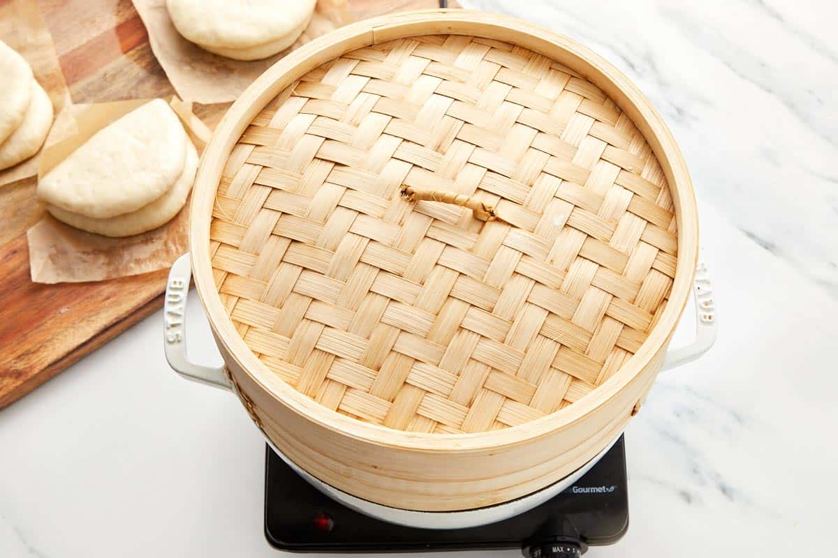 Bamboo steamer with bao buns resting nearby on parchment squares.