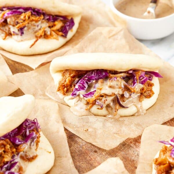 Steamed bao buns filled with pulled pork, red cabbage, and drizzled black garlic mayo on parchment paper.