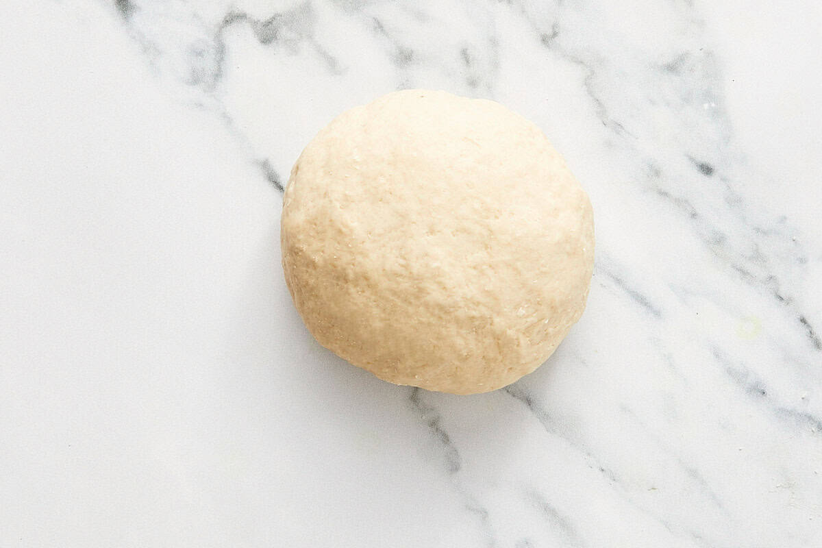 Smooth ball of bao dough on a marble surface, ready to rise.