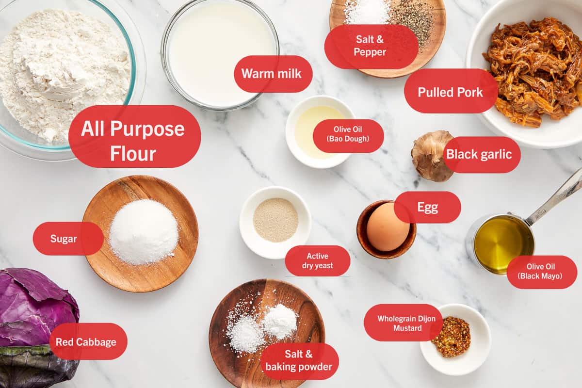 Flat lay of labeled ingredients for bao buns with black garlic mayo, including flour, warm milk, pulled pork, red cabbage, black garlic, and spices.
