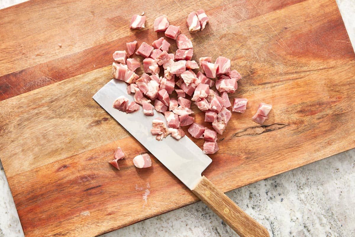 Raw pancetta cut into small cubes on a wooden cutting board, ready to be crisped.