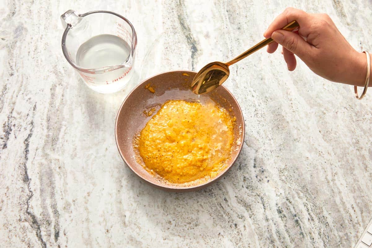 Hot pasta water being whisked into the yolk and cheese mixture.