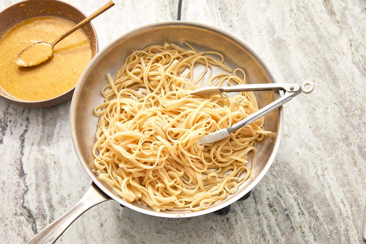 Cooked linguini in a skillet next to a bowl of carbonara