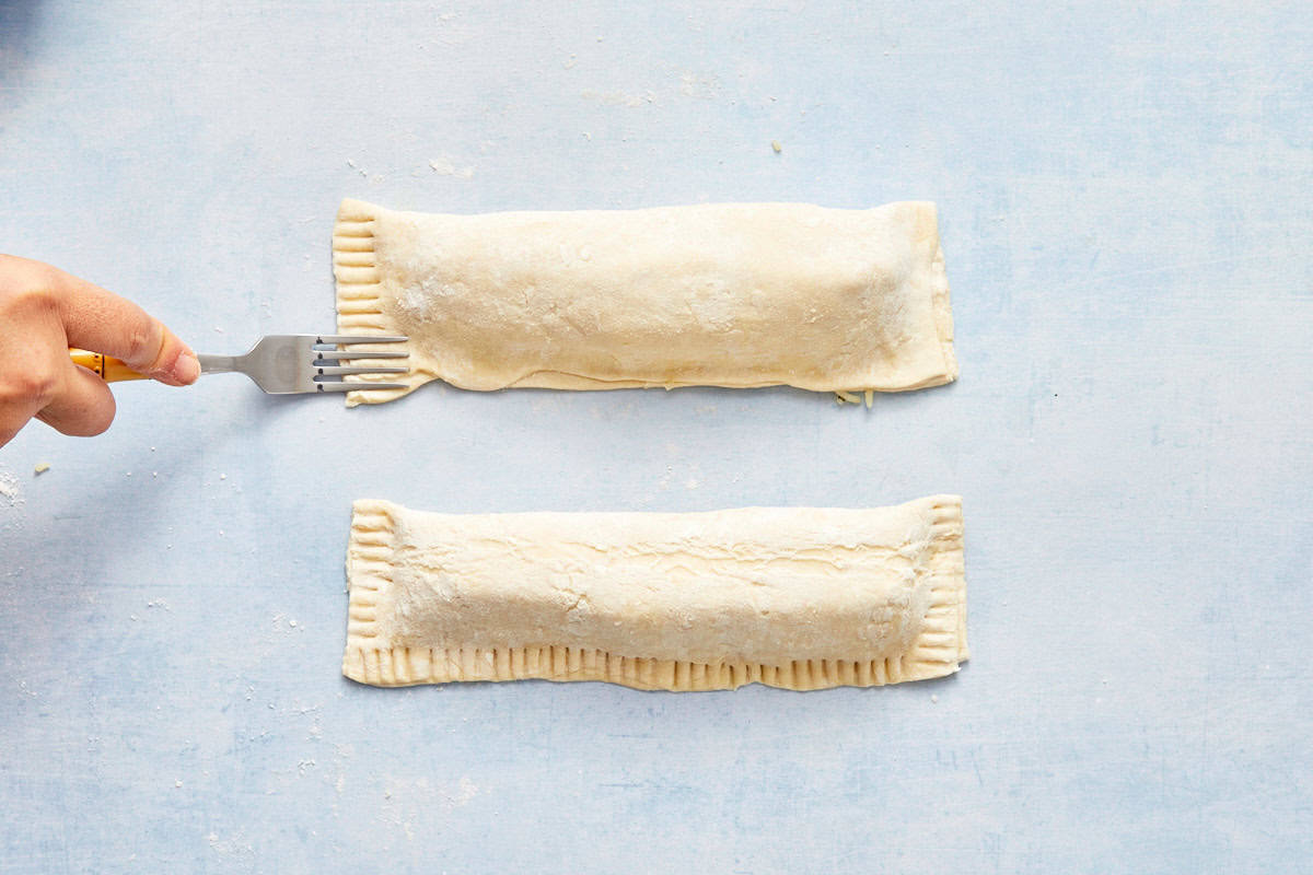 Fork pressing the edges of the puff pastry parcel to seal it.