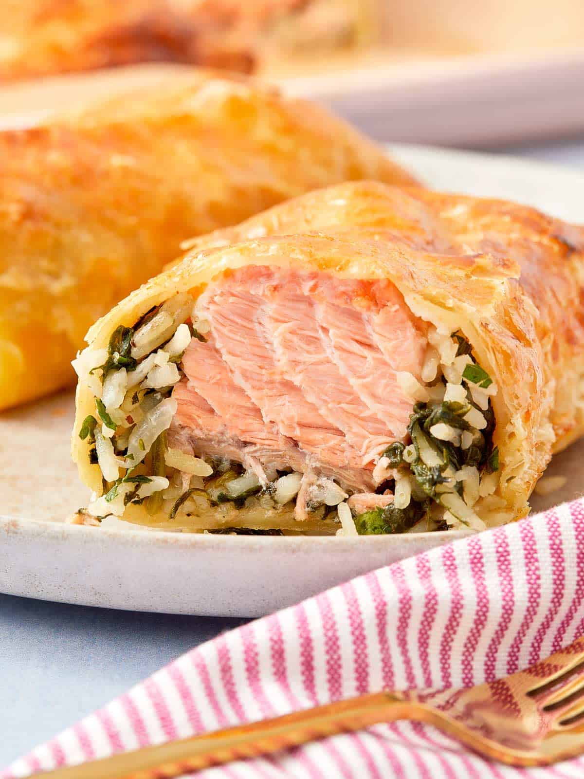 Close-up of a golden Puff Pastry Salmon Parcel sliced open to reveal flaky salmon, creamy spinach, and rice inside.