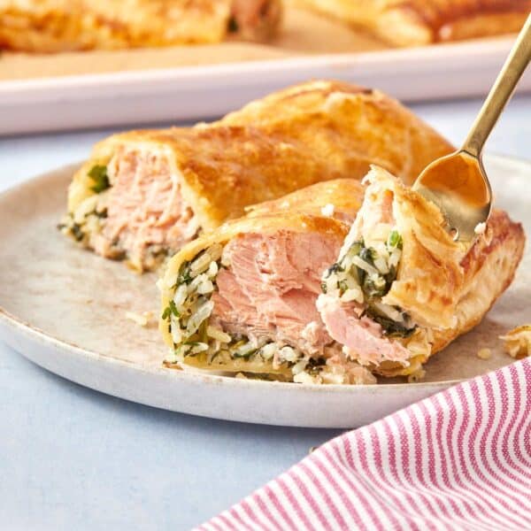 Serving a Puff Pastry Salmon Parcel on a plate, showing the crispy layers and juicy salmon filling being picked up with a fork.