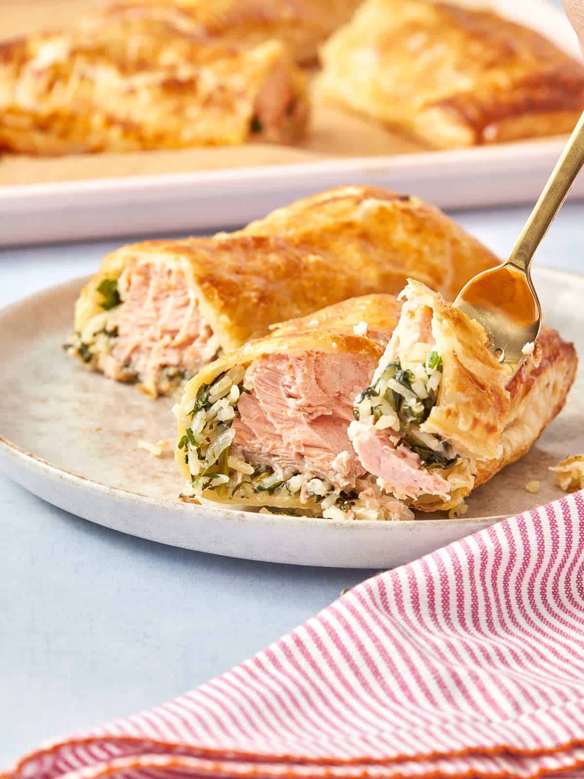 Serving a Puff Pastry Salmon Parcel on a plate, showing the crispy layers and juicy salmon filling being picked up with a fork.