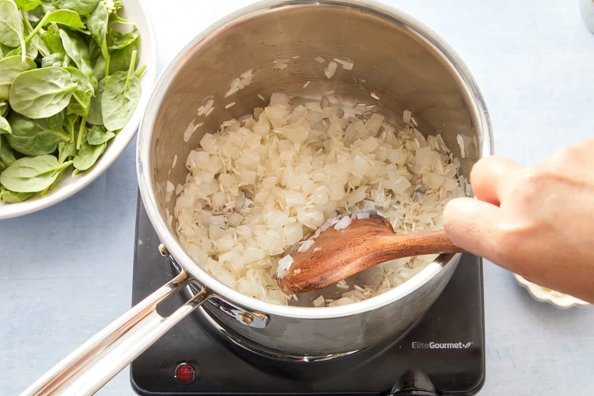 Stirring spinach and garlic into softened onions in a pot.