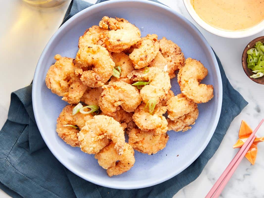 Plate of golden-fried shrimp garnished with sliced green onions, sauce and garnish bowls nearby.