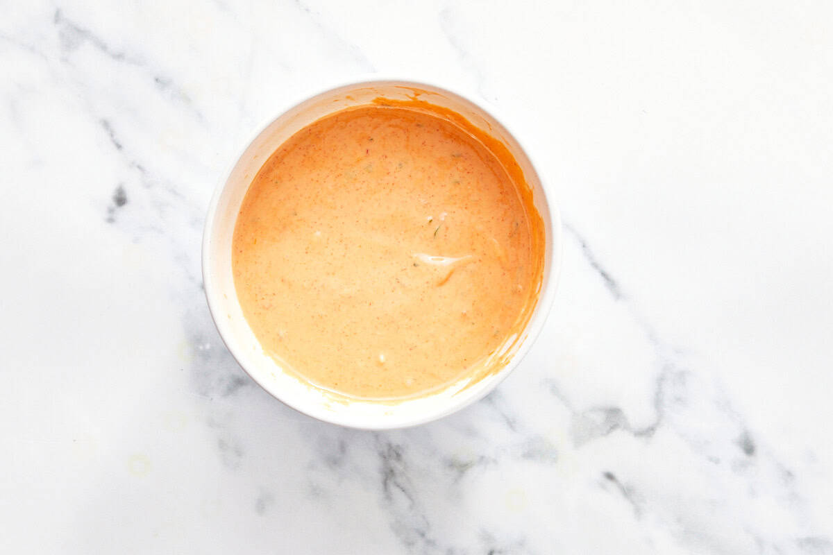 Bowl of creamy orange Bang Bang sauce on a marble surface.