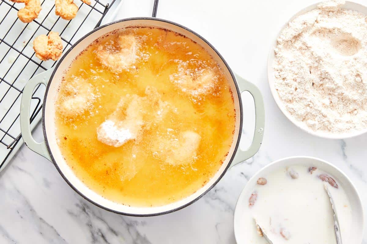 Shrimp frying in hot oil in a large pot, with coated shrimp and a rack of cooked shrimp on the side.