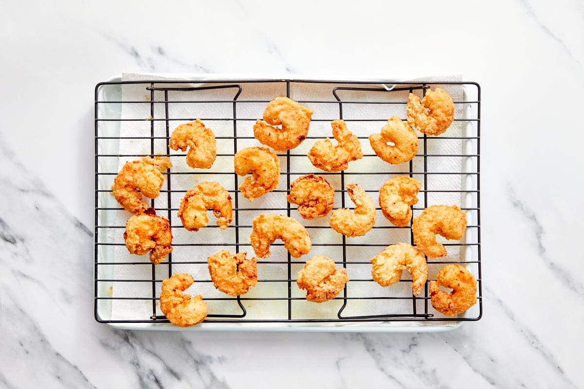 Fried shrimp arranged on a wire rack over paper towels to drain excess oil.