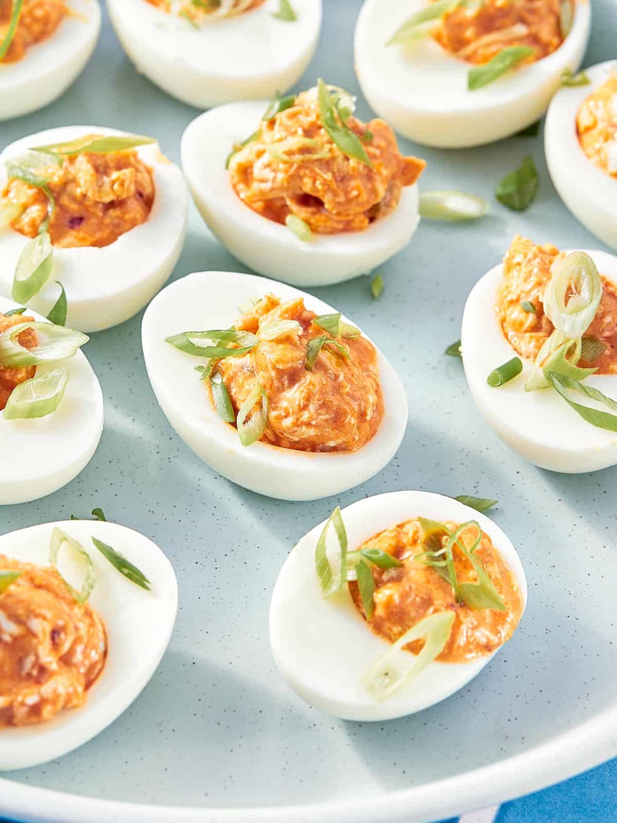 Buffalo chicken deviled eggs topped with green onion on a plate.