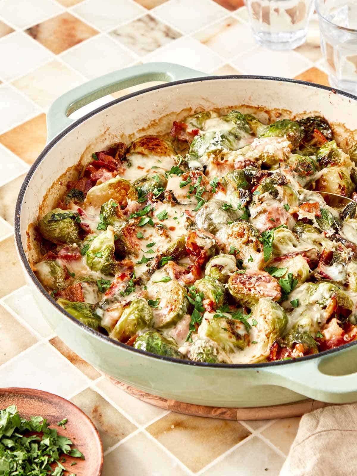 Creamy garlic parmesan Brussels sprouts with bacon bubbling in a skillet, topped with melted cheese and fresh parsley